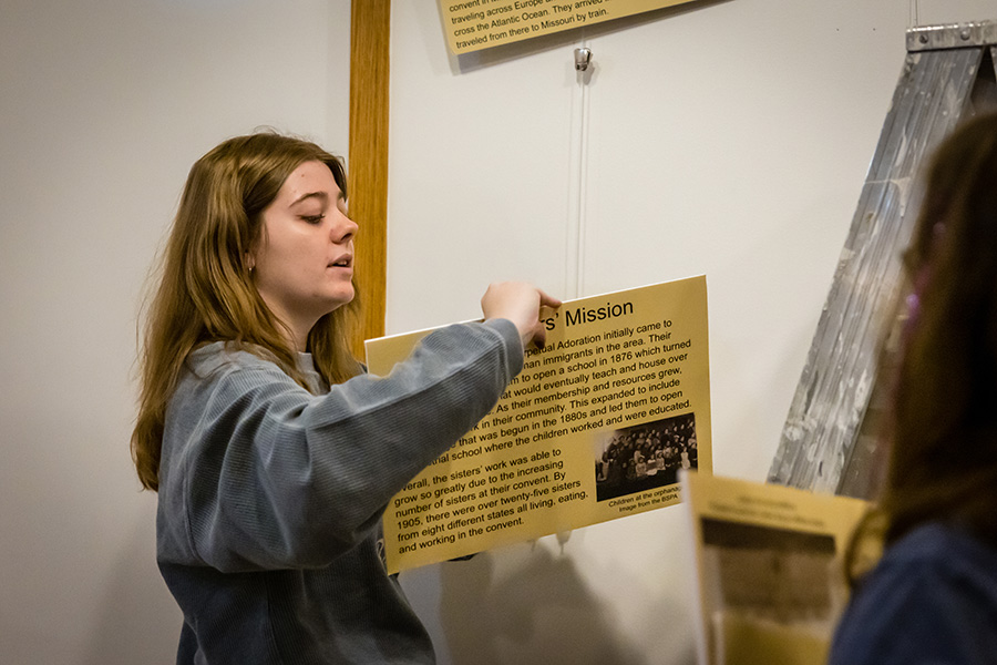 Northwest student Emma Everly hangs a display panel with information about the Benedictine Sisters of Perpetual Adoration. (Photo by Lilly Cook/Northwest Missouri State University)